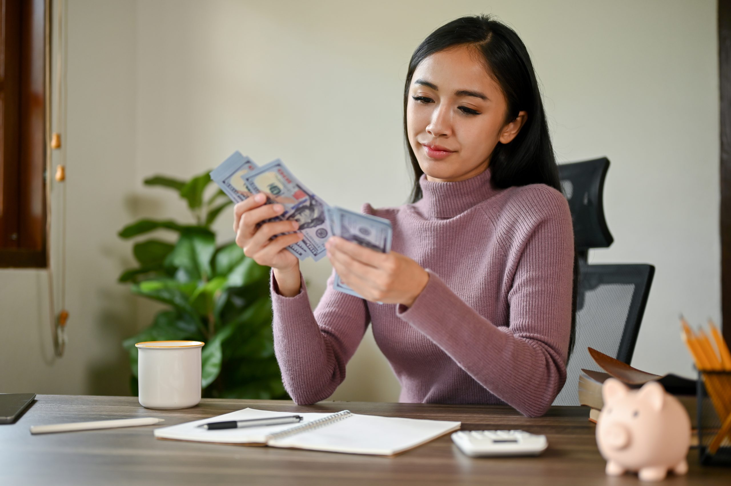 A beautiful Asian female counting her money at a table planning her savings